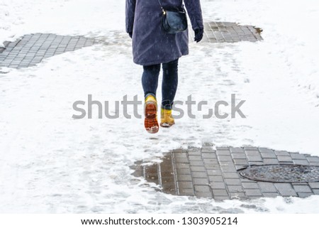 Winter Walk in Yellow Leather Boots. Back view on the feet of a women walking along the icy snowy pavement. Pair of shoe on icy road in winter. Abstract empty blank winter weather background