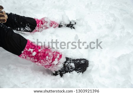 The teenage girl is sitting  in a park covered with snow,.  Close-up of snow-covered girl's legs.