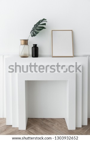 Composition of empty gold frame & artificial plant in glass vase with gold stainless trim edge and gold mirror vase setting on empty  fireplace in minimal modern style /empty space fo advrtisement