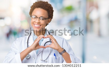 Young african american doctor woman wearing medical coat over isolated background smiling in love showing heart symbol and shape with hands. Romantic concept.