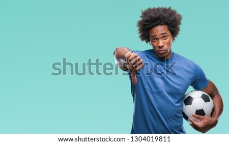 Afro american man holding football ball over isolated background with angry face, negative sign showing dislike with thumbs down, rejection concept