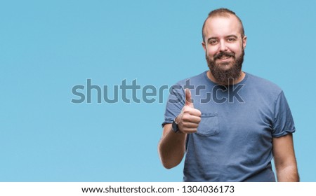 Young caucasian hipster man over isolated background doing happy thumbs up gesture with hand. Approving expression looking at the camera with showing success.