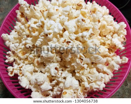 CLOSE UP OF A PINK RECIPE FULL OF TASTY POPCORNS READY TO BE EATEN. CLASSICAL SALTY POPCONS. HORIZONTAL PHOTO 