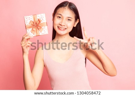 Asian woman show victory sign with a gift box on pink background