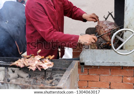 Turkish Cag Kebab cooking in a BBQ. Cook slicing the meat with a knife. - Image