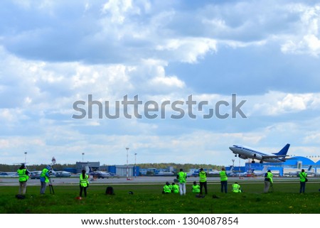 Spotters in yellow vests, photographers, take pictures of a commercial passenger plane taking off from the airport