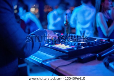 Dj mixing at party festival with crowd of people dancing in background.