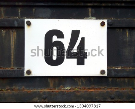 Address marker house number 64: sign with black digits against rusty black metal door
