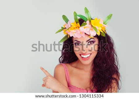 Smiling woman pointing finger to side copyspace, saying look right here. Colombian latin hispanic mixed race model in floral crown on head brunette curly hair isolated on  light green gray background