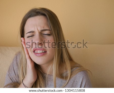 Young blonde girl with brackets or braces feels pain. She has her hand on her face and she expresses pain.