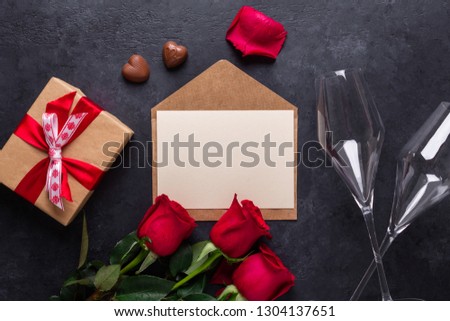 Red rose flowers bouquet, envelope, gift box, chocolate sweets, champagne glasses on black stone background Valentine's day greeting card Copy space Top view