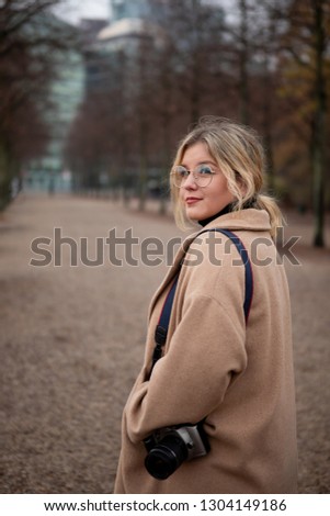 Portrait of smiling woman in glasses enjoying city view on a street of Berlin, Germany. Girl having fun in the city in Europe with camera. A young photographer walks through the city streets.