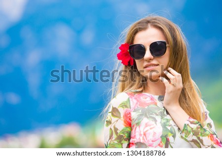 Beautiful girl with floral dress and sunglasses standing, in background are The Alps in Italy. Amazing view. Summer time.