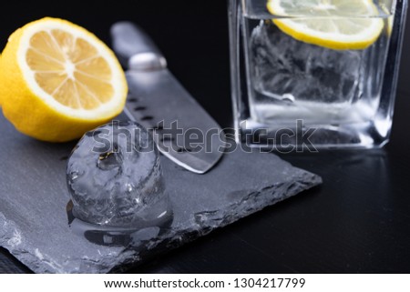 Cold drink in a glass on the kitchen table. Lemon and ice with water the best way to cool off on a summer day. Dark background.