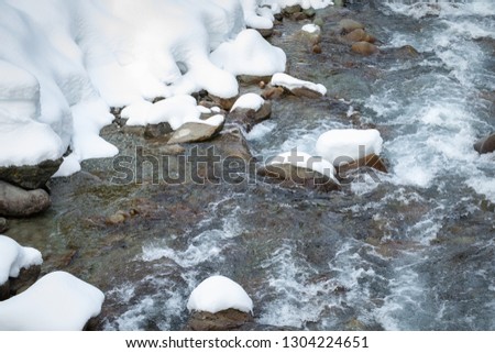 Close up on glacier melt water flowing down a mountain creek, with snow on the  river rocks and riverbanks