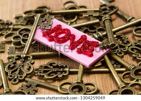 conceptual image using old keys with a pink tag with red glitter letters spelling the word love over a wooden background