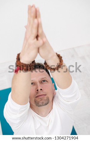 Male brunette with a beard in white clothes on a white background with his hands folded on his chest. Meditation and prayer, yoga.
