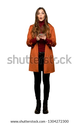 Full-length shot of Young woman with coat surprised and sending a message on isolated white background