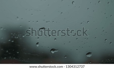 Water Droplets on a window while the car is outside with blurred structures behind the window