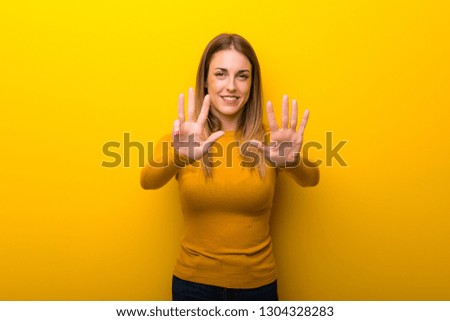 Young woman on yellow background counting nine with fingers