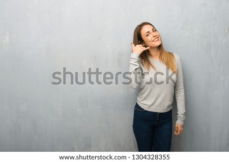 Young woman on textured wall making phone gesture. Call me back sign