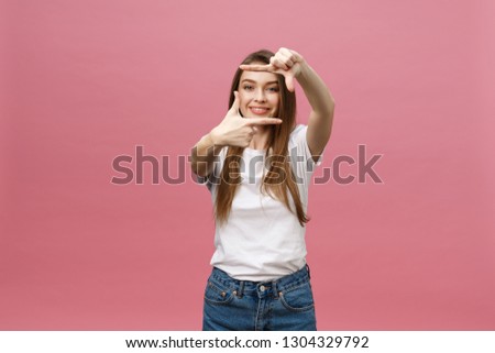 Cheerful young woman keeping mouth wide open, looking surprised, making hands photo frame gesture isolated on bright pink background.