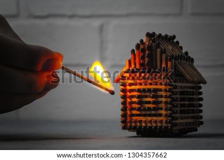 hand with a burning match sets fire to the house model of matches, risk, property Insurance protection or ignition of combustible materials concept Royalty-Free Stock Photo #1304357662