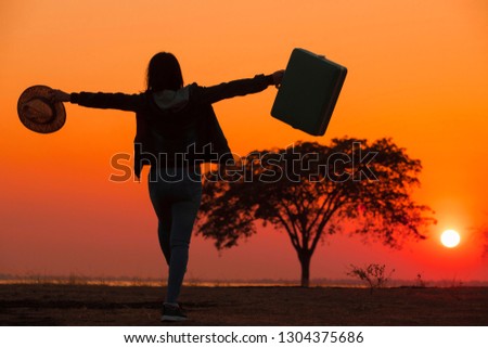 Woman with suitcase, young woman with suitcase standing in the  field,Women spread their arms happy with the view in front of the sunset.The silhouette of tourists and luggage