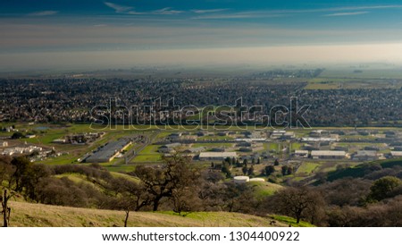 Panoramic view Vacaville and the state prison from the Lagoon Valley Park, California, USA, featuring the chaparral in the winter with green grass, and hazy sky Royalty-Free Stock Photo #1304400922