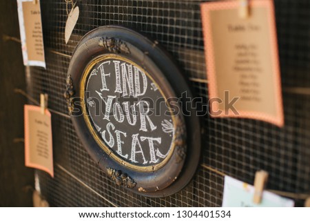 Wedding ceremony sign "Find Your Seat" hanging on wall near the ceremony location. 