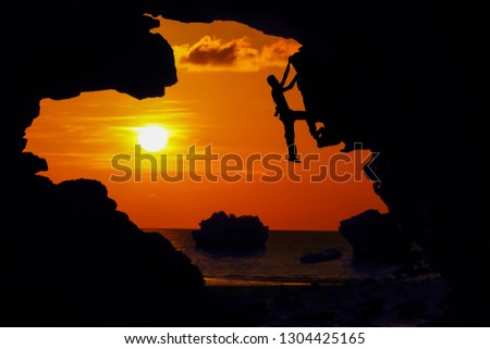 Photographer climbing rock in the cave near the beach with kayaking and red sky sunset.