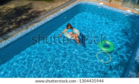 Aerial view of beautiful girl in swimming pool from above, swim on inflatable ring donut and has fun in water on family vacation on tropical holiday resort