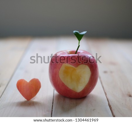 Red apple with a heart shaped cut-out on wood background. Healthy eating.