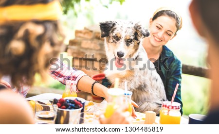 Happy friends on healthy pic nic breakfast at countryside farm house - Young people millennials with cute dog having fun together outdoors at garden party - Food and beverage lifestyle concept