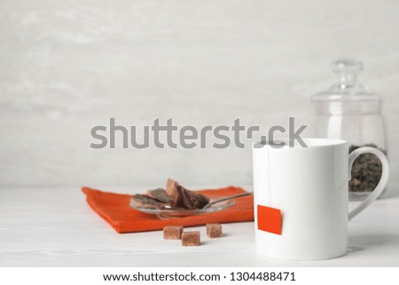 Cup of hot fresh tea and brown sugar on table against light background. Space for text