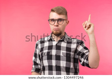 Attractive funny young man wearing eyeglasses and plaid shirt pointing up with his finger isolated on pink background