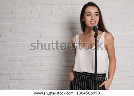 Young woman in casual clothes posing with microphone near brick wall. Space for text