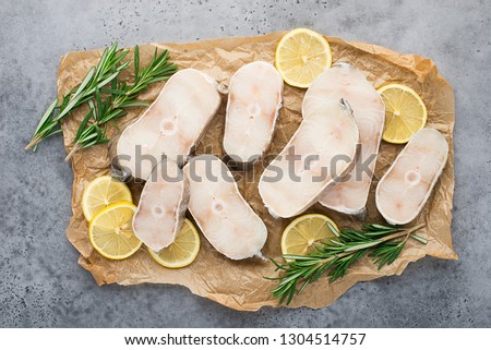 Sea white fish cod steaks raw on paper with sprigs of rosemary and lemon slices on a light gray background. Top view