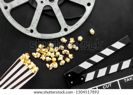 Movie premiere concept. Clapperboard, film stock, popcorn on black background top view