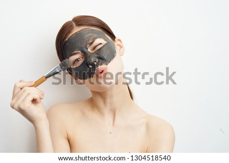 young woman holds brush on face cosmetic mask made of clay