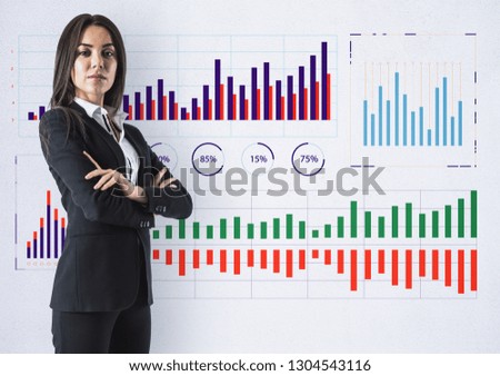 Attractive young businesswoman standing on concrete wall background with business charts sketch. Finance and economy concept 