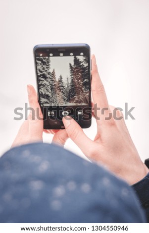 Woman takes pictures of the winter forest by mobile phone and trees are on smartphone screen