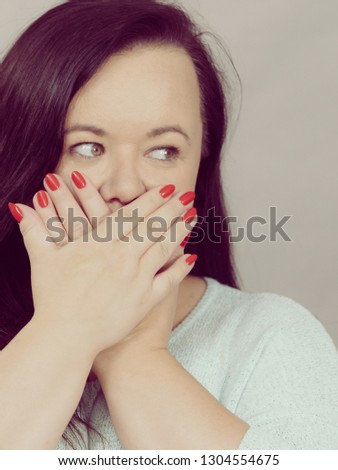 Adult woman showing silence, shame gesture having hands on covering her mouth. Studio shot on grey background.