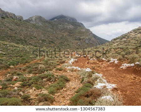 Stony walking trail or footpath marked with white, running through a wild landscape, downhill towards the famous Balos blue Lagoon with Cape Tigani in Crete island, Greece. Royalty-Free Stock Photo #1304567383