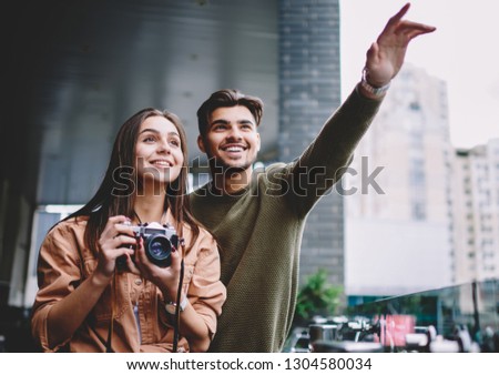 Cheerful couple in love spending travel vacations together on date using camera for making photos, happy handsome man pointing on smith showing to his girlfriend while teaching photography outdoors