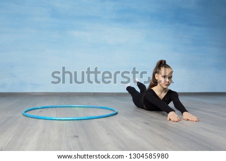 Girl gymnast in a black gymnastic swimsuit warming up before training, on the floor is a gymnastic hoop.