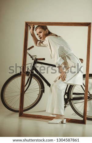 attractive stylish girl in white outfit posing with bicycle and big wooden frame