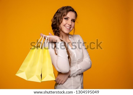 Picture of beautiful smiling young woman in white blouse holding cruft bags after shopping