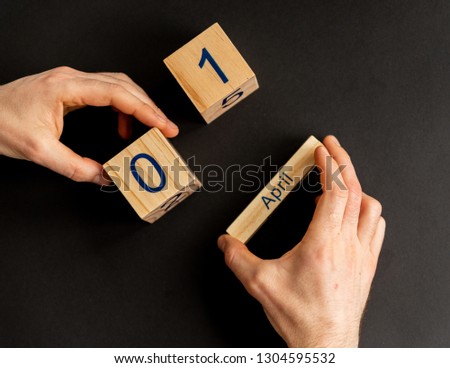 Above view of male holding in hands three wooden cubes with figure of 1 of April. Concept of symbol International Day of Smile and humor and first day of April. Black studio background.