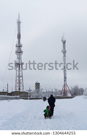 Father with children on a sled goes to TV tower and cell tower in the fog. Misty winter morning.